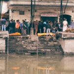 A traditional funeral ceremony taking place by a riverside in an urban setting.