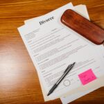 Flat lay of divorce papers with a pen and ring on a wooden table for legal themes.