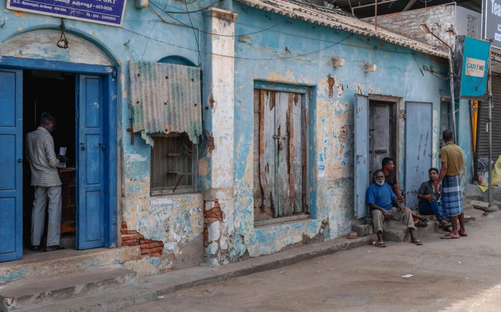 Local residents gather outside rustic buildings in Thanjavur, India, capturing daily life.