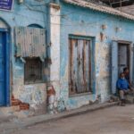 Local residents gather outside rustic buildings in Thanjavur, India, capturing daily life.