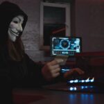 Masked hacker with credit card at computer, symbolizing cybercrime and anonymity.