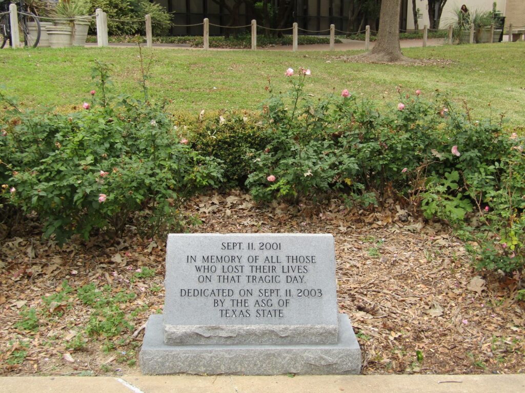 Memorial stone for 9/11 victims surrounded by roses in a peaceful park.