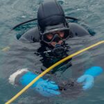 A professional diver in wetsuit and scuba gear holding a sea urchin in the ocean.