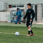 A young soccer player in training gear practices on a grassy field.