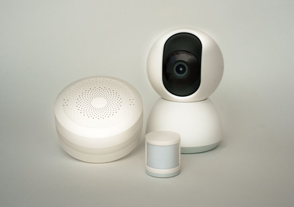 Modern smart home devices including a camera and sensors on a neutral background.