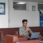 Smiling young adult sitting with laptop in a modern office lounge, focusing on work.