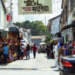 Colorful street market in George Town, Penang, bustling with locals and tourists under a bright sky.