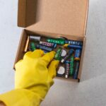 Yellow-gloved hand handling used batteries for safe recycling.