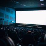 A crowded cinema audience seated in a theater watching a movie on a large screen.