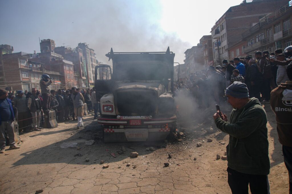 A crowd gathers around a smoky truck in a busy urban street, capturing the scene.