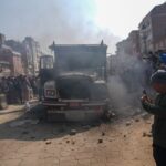 A crowd gathers around a smoky truck in a busy urban street, capturing the scene.