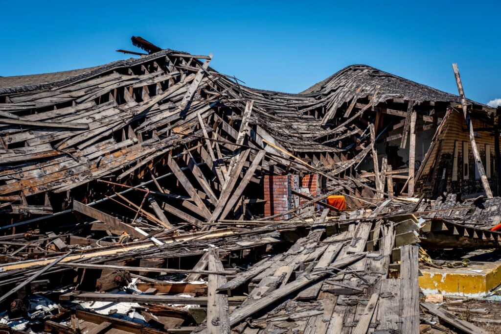 A dramatic view of a destroyed wooden building after a catastrophe, showing debris and structural failure.