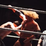 Dramatic wrestling scene with referee coaching competitors in the ring.
