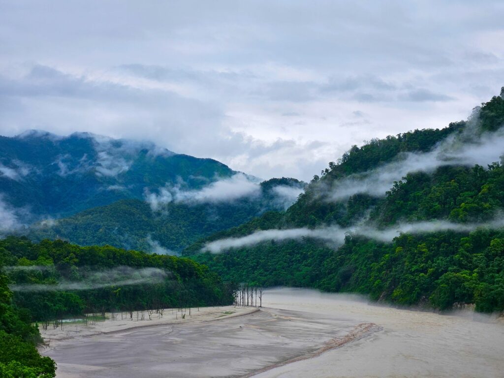 Captivating landscape of mist descending over a tranquil river and lush green hills.