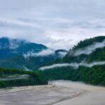 Captivating landscape of mist descending over a tranquil river and lush green hills.