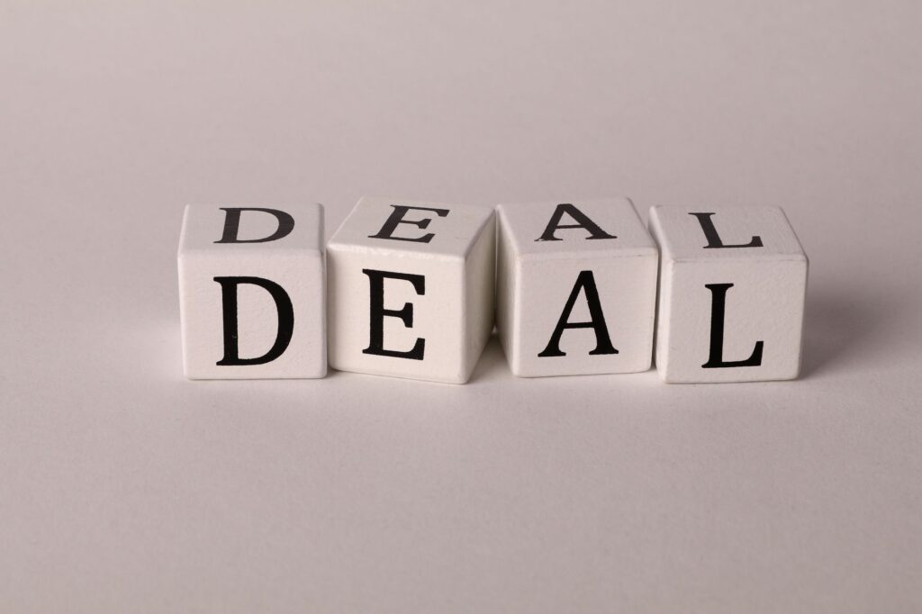 Close-up of white cubes with black letters spelling DEAL on a plain background.