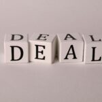 Close-up of white cubes with black letters spelling DEAL on a plain background.