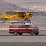 Unique scene of yellow plane mounted on red van, outdoors.