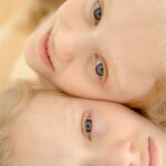 Delightful portrait of twin girls with blond hair, close-up view highlighting their joyful expressions and togetherness.
