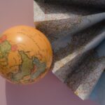 A globe and a folded map on a pink background, showcasing geography and cartography.