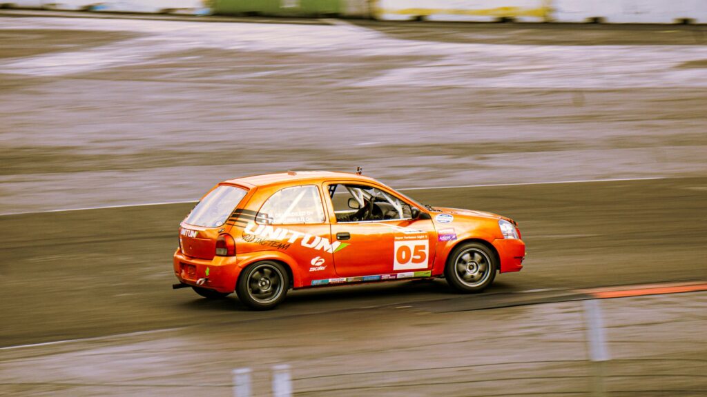 Vibrant orange sports car racing on a smooth asphalt track at high speed.