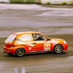Vibrant orange sports car racing on a smooth asphalt track at high speed.