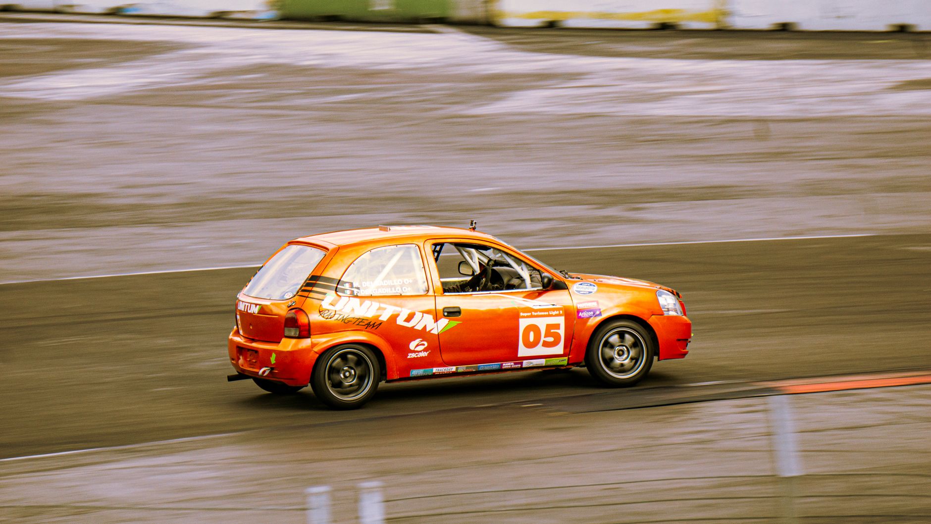 Vibrant orange sports car racing on a smooth asphalt track at high speed.