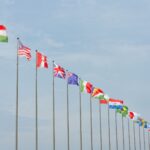 A series of international flags flying in a line against a clear blue sky, symbolizing global unity.
