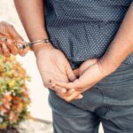 Close-up of hands in handcuffs during an arrest by police officer outdoors.
