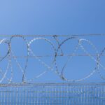 Detailed image of barbed wire fence under clear blue sky, symbolizing security and restriction.