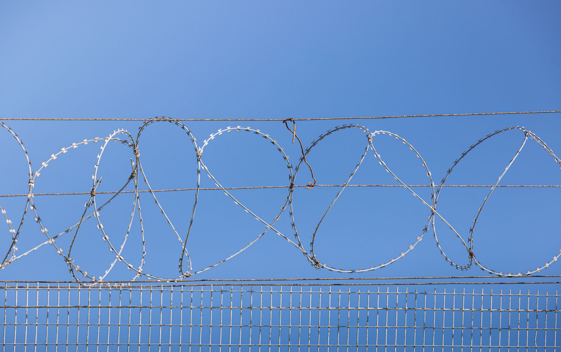 Detailed image of barbed wire fence under clear blue sky, symbolizing security and restriction.