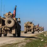 American military convoy driving through rural Syria under a blue sky.