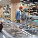 Diverse couple shopping in a supermarket, exploring frozen produce aisle together.