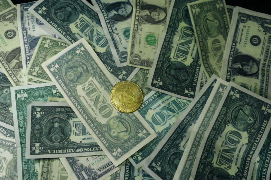 A golden bitcoin coin surrounded by scattered US dollar bills, symbolizing the contrast between digital and traditional currency.