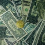 A golden bitcoin coin surrounded by scattered US dollar bills, symbolizing the contrast between digital and traditional currency.