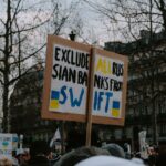 Crowd gathered with placards during a protest against Russian banks in an urban setting.