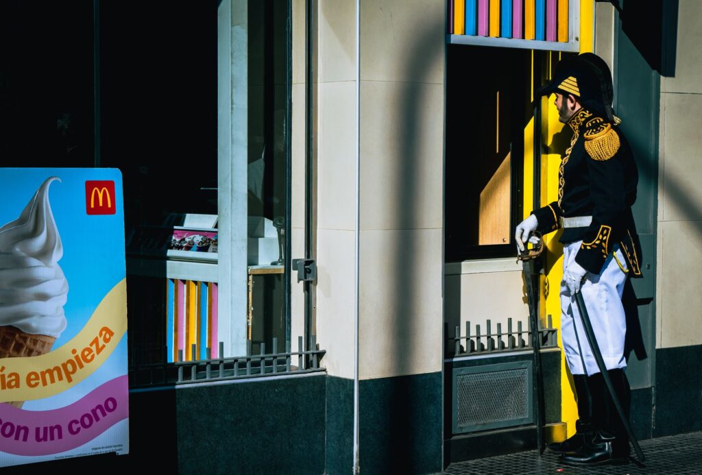 A man in historical military uniform stands outside a fast food outlet, blending past and present.