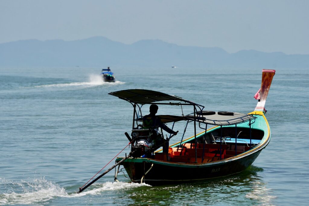 Longtail boat with silhouette of a person navigating the calm sea, distant islands in view.