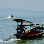 Longtail boat with silhouette of a person navigating the calm sea, distant islands in view.
