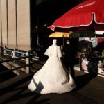 A bride and groom walk along the Istanbul waterfront, casting long shadows in the evening sun.