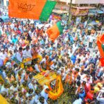 Crowds gather in Mangaluru for a colorful street parade with vibrant flags and decorations.