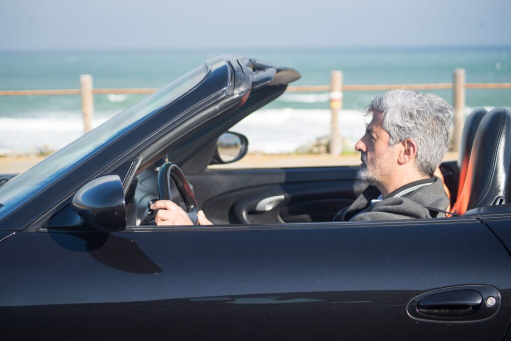 Senior man with gray hair drives a convertible along the scenic Portuguese coast.