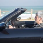 Senior man with gray hair drives a convertible along the scenic Portuguese coast.