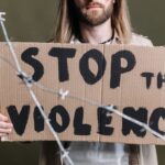 Close-up of a protester holding a cardboard sign reading 'Stop the Violence' with barb wire in focus.
