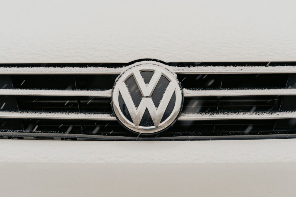 Closeup of a snow-dusted Volkswagen car grille shows the iconic VW logo.