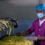 A factory worker in protective gear monitors the production of French fries, ensuring quality control.