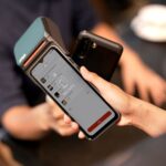 Close-up of a smartphone making a contactless payment at a modern payment terminal in a retail environment.