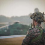 A soldier in camouflage stands with a helicopter in the background, Kolkata, India.