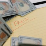 Close-up of US dollars and 'Fraud' written on yellow paper, representing financial scams.