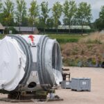 Wind turbine component at a construction site, surrounded by equipment and rural landscape.
